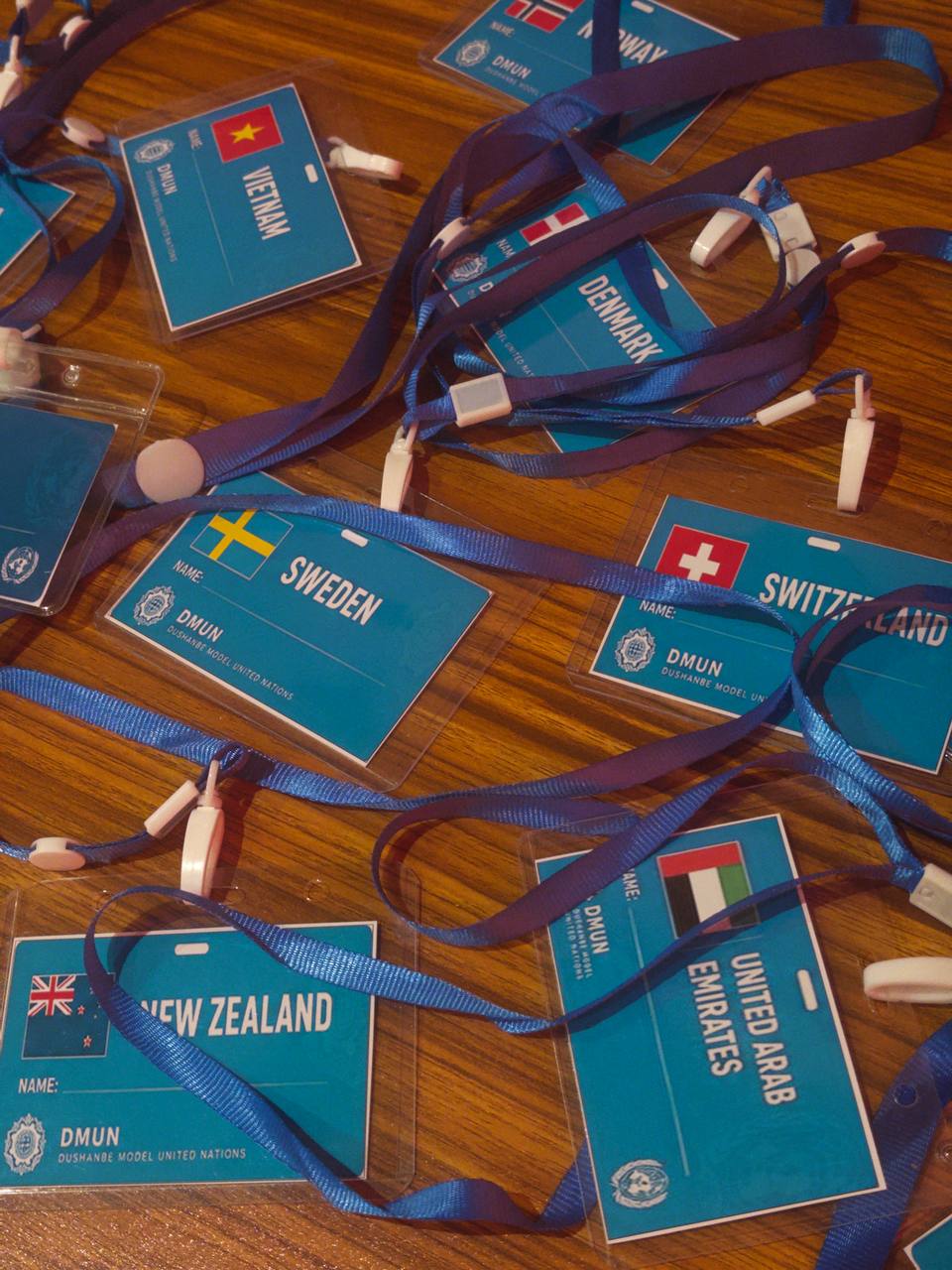 DMUN delegate badges with country names and lanyards laid out on a wooden table.